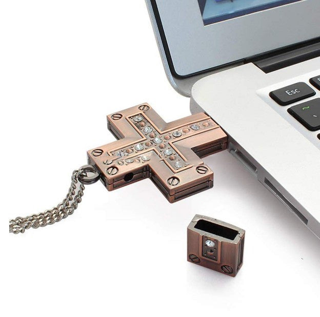Golden metal cross USB flash drive connected to a laptop USB port with decorative stones and a cap on the side.