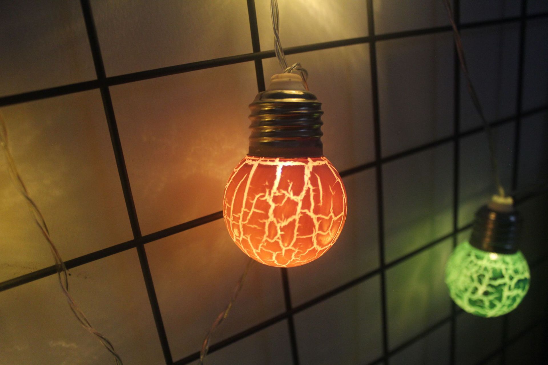 LED string lights with cracked bulb design hanging against a tiled wall, glowing in warm orange and green colors